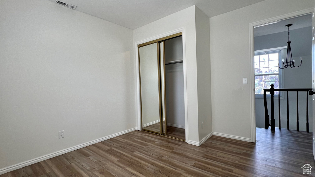 Unfurnished bedroom featuring dark wood-style flooring, a chandelier, a closet, and baseboards