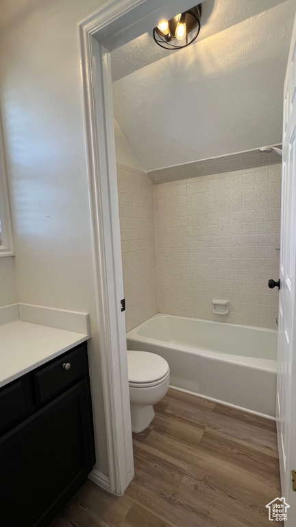 Bathroom featuring wood finished floors, toilet, vanity, lofted ceiling, and  shower combination