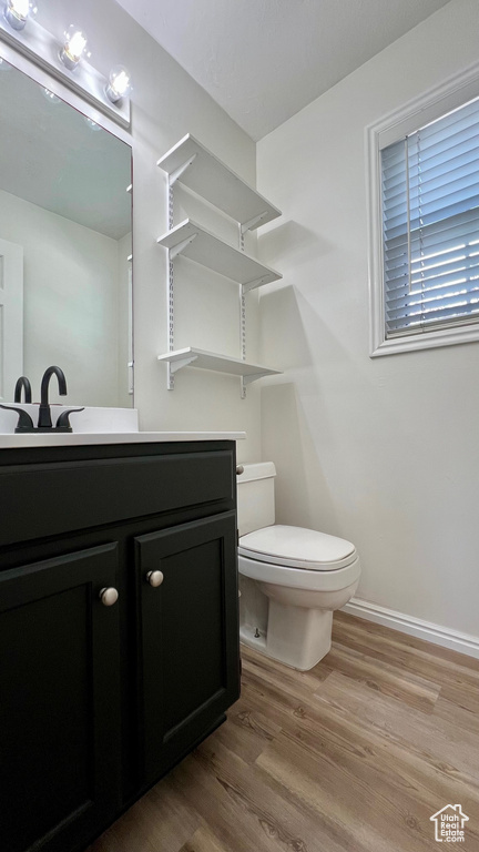 Half bathroom featuring toilet, vanity, wood finished floors, and baseboards