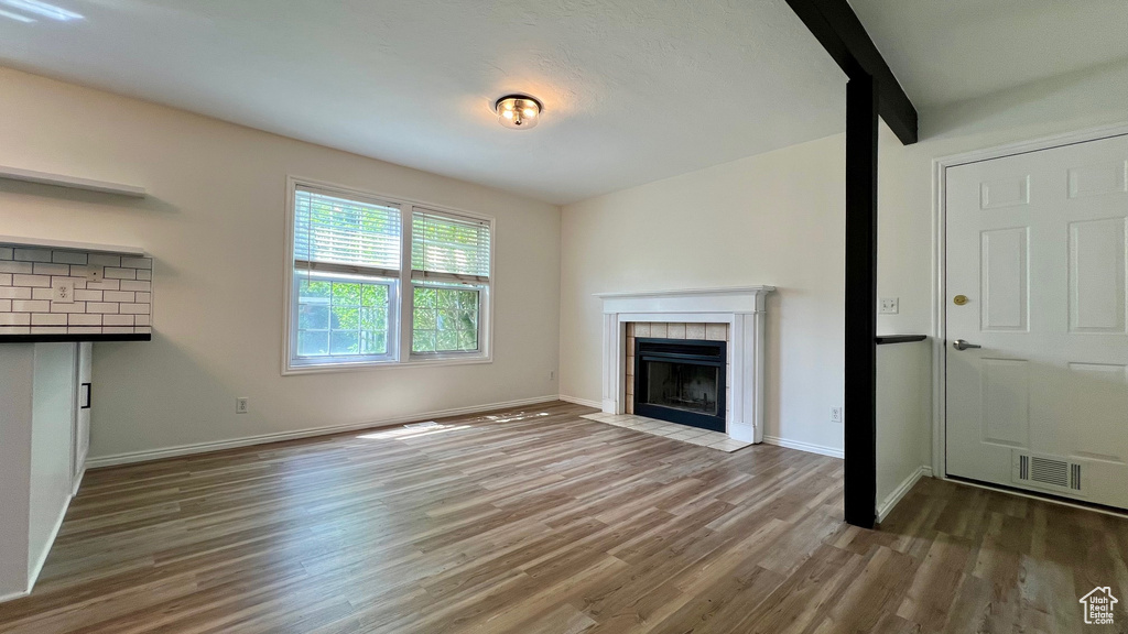 Unfurnished living room with wood finished floors, a tile fireplace, and baseboards