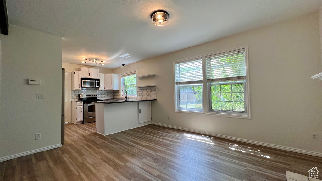 Kitchen featuring appliances with stainless steel finishes, a peninsula, wood finished floors, and white cabinets