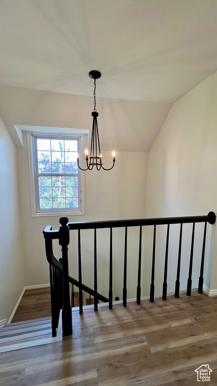 Stairs with a chandelier, wood finished floors, baseboards, and lofted ceiling