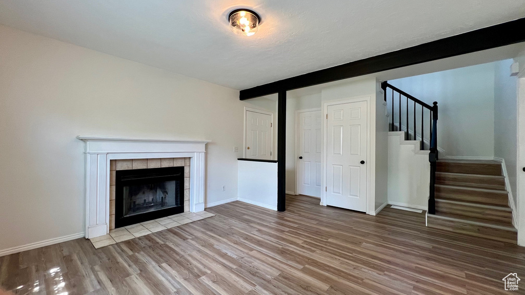 Unfurnished living room featuring wood finished floors, stairs, a fireplace, baseboards, and beamed ceiling