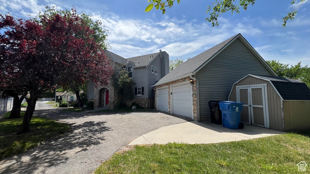 View of side of home with asphalt driveway, a garage, and roof with shingles