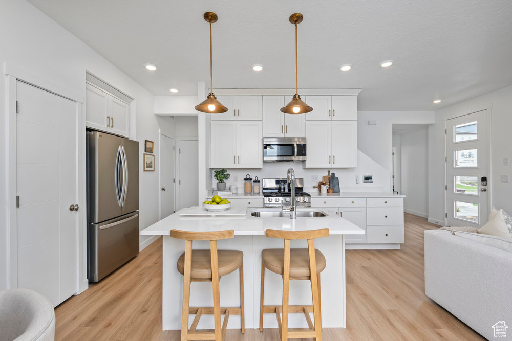 Kitchen featuring appliances with stainless steel finishes, light wood-type flooring, light countertops, white cabinets, and recessed lighting