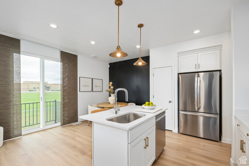 Kitchen with stainless steel appliances, a sink, light wood-style flooring, light countertops, and decorative light fixtures