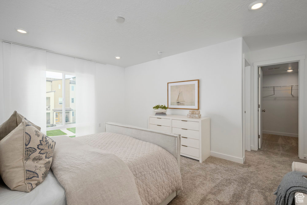 Bedroom with light colored carpet, recessed lighting, a walk in closet, and baseboards