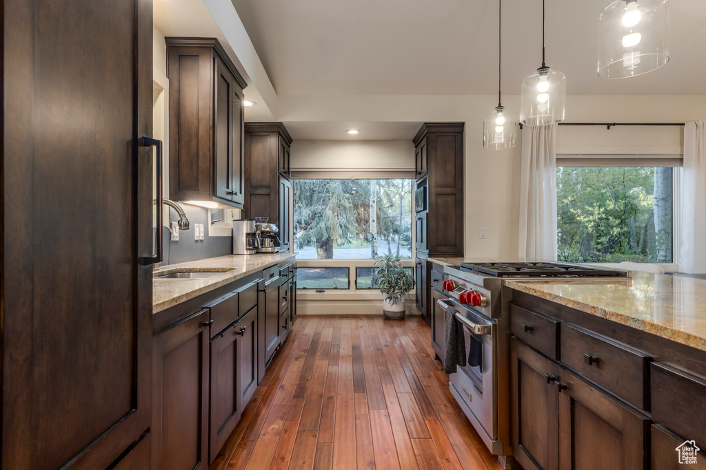 Kitchen with stainless steel appliances, a sink, dark brown cabinetry, light stone countertops, and healthy amount of natural light