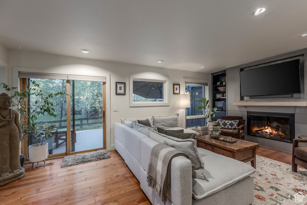 Living area featuring light wood finished floors, a glass covered fireplace, recessed lighting, and built in features