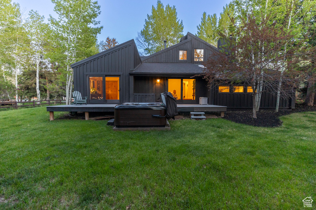 Rear view of house featuring a hot tub, board and batten siding, a yard, a chimney, and a deck