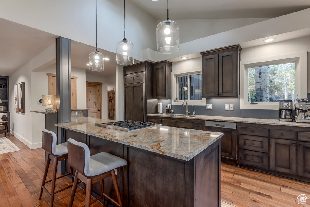 Kitchen with stainless steel gas cooktop, dark brown cabinetry, a sink, a kitchen bar, and light wood-type flooring
