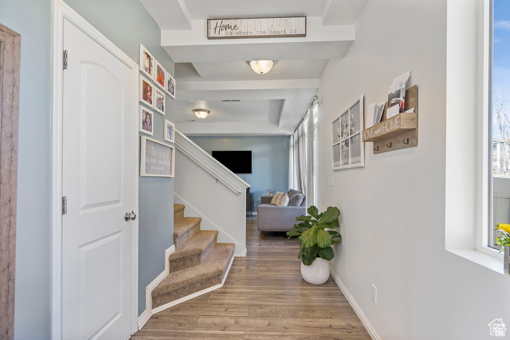 Corridor featuring wood finished floors, stairway, baseboards, plenty of natural light, and beamed ceiling