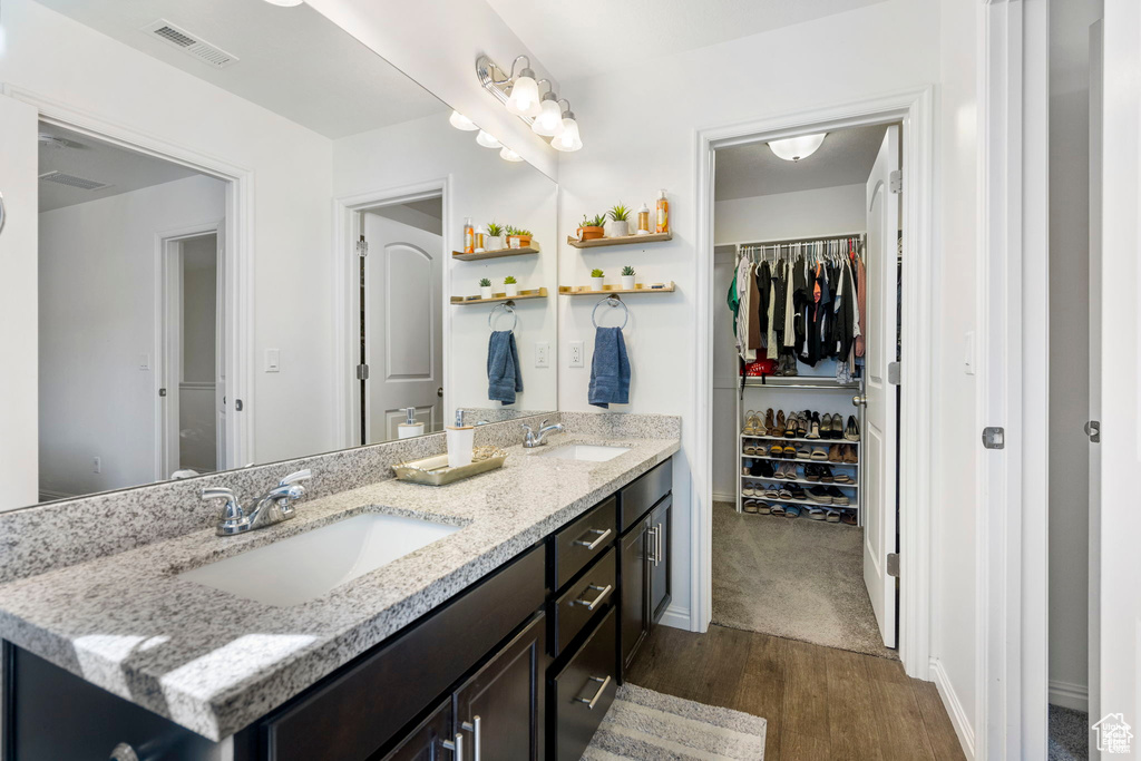 Bathroom with wood finished floors, double vanity, a walk in closet, and baseboards