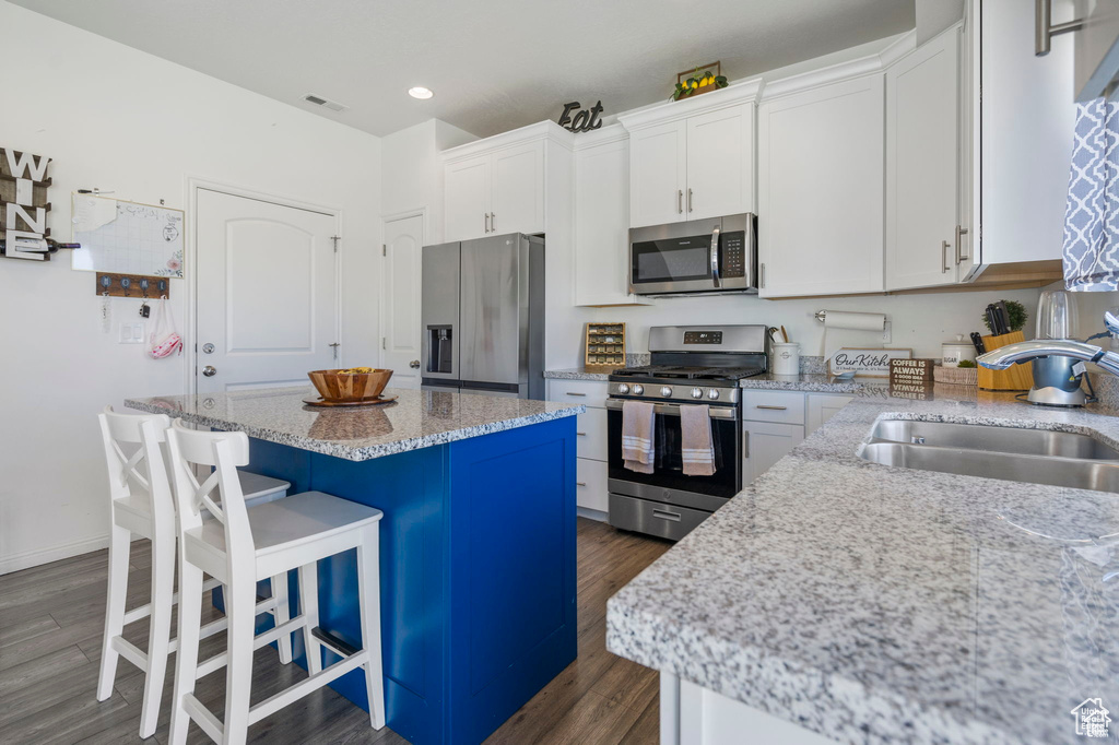 Kitchen featuring stainless steel appliances, a sink, dark wood-style floors, a kitchen bar, and a kitchen island