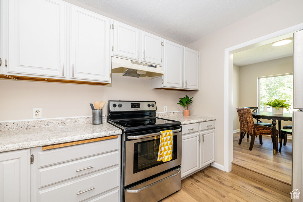 Kitchen featuring under cabinet range hood, stainless steel electric range, light wood-style flooring, and white cabinetry
