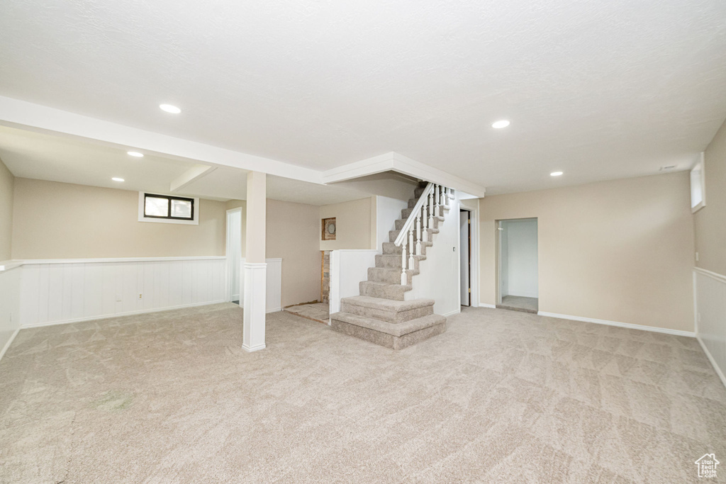 Below grade area with carpet flooring, recessed lighting, stairs, and a wainscoted wall