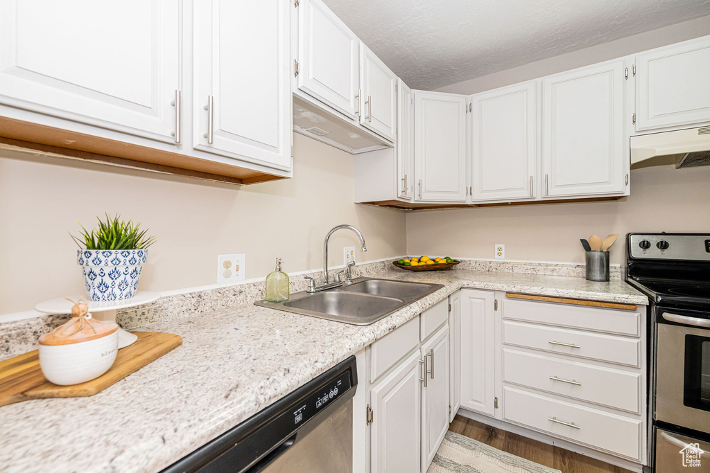 Kitchen featuring stainless steel appliances, under cabinet range hood, white cabinetry, light countertops, and light wood-type flooring