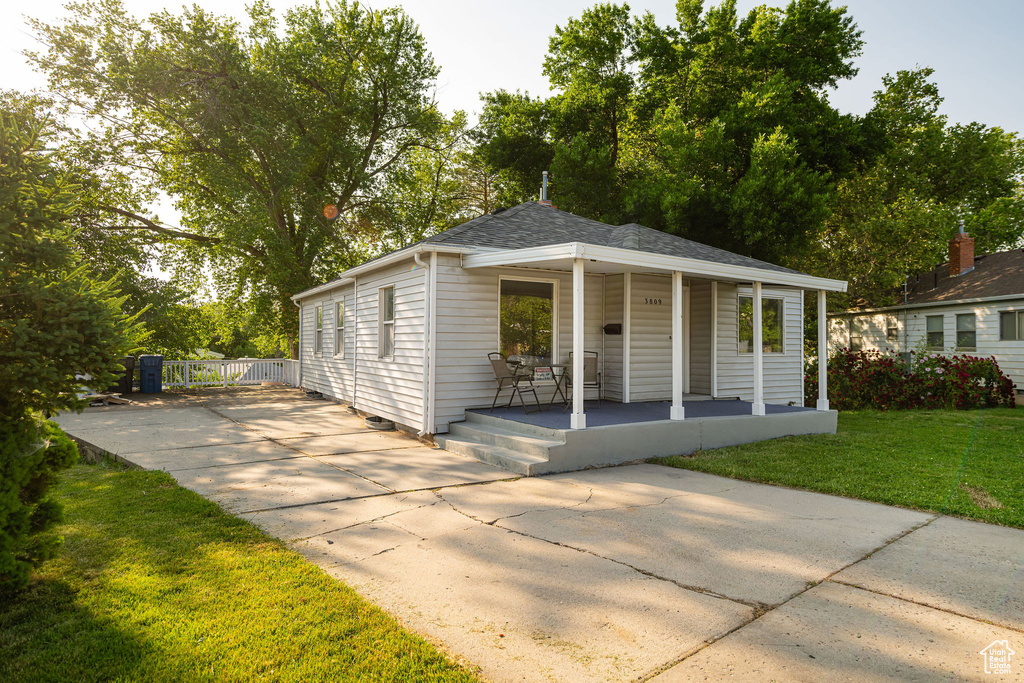 View of front of property with covered porch, a front yard, concrete driveway, and a shingled roof