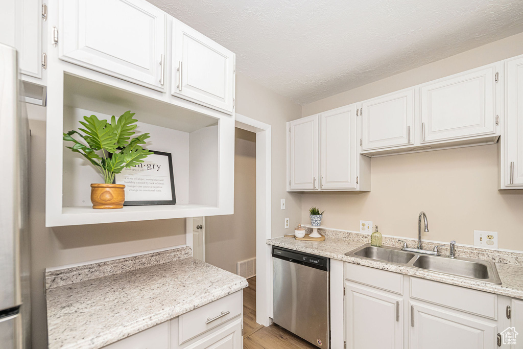 Kitchen with stainless steel dishwasher, light wood-type flooring, light countertops, white cabinets, and a textured ceiling