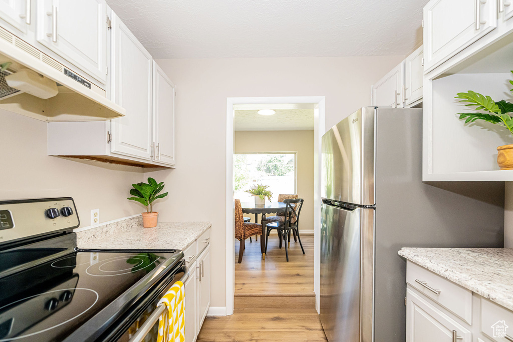 Kitchen featuring stainless steel appliances, under cabinet range hood, white cabinets, and light wood finished floors