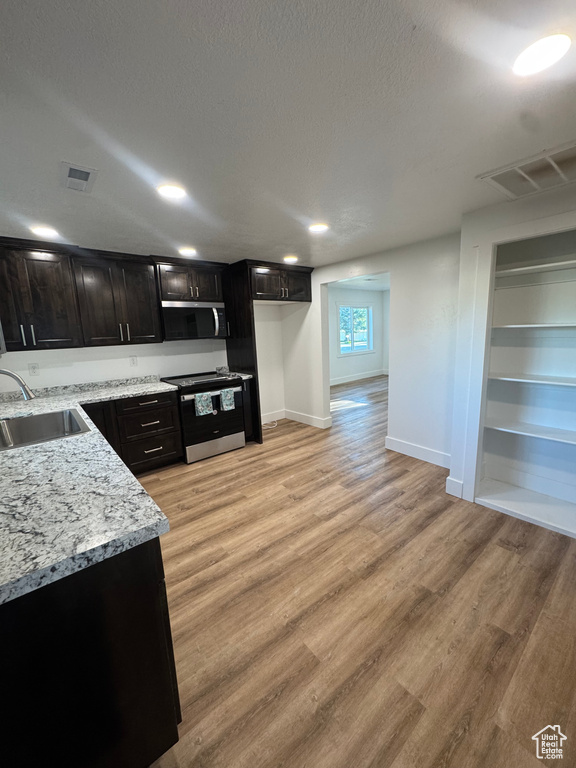 Kitchen featuring appliances with stainless steel finishes, a sink, baseboards, light wood finished floors, and light stone countertops