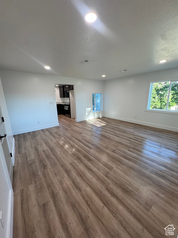 Unfurnished living room featuring dark wood-type flooring, baseboards, a textured ceiling, and recessed lighting