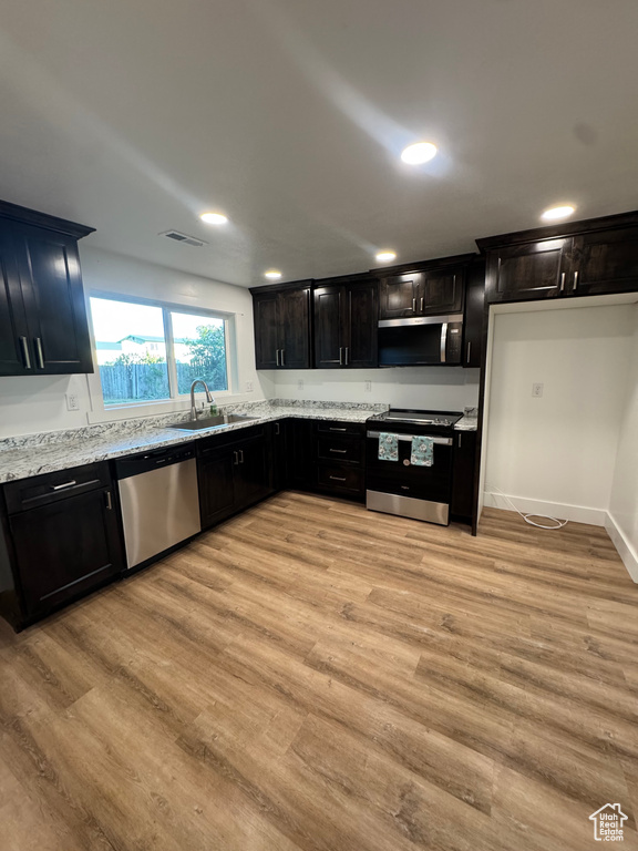 Kitchen featuring stainless steel appliances, light wood finished floors, light stone counters, a sink, and recessed lighting