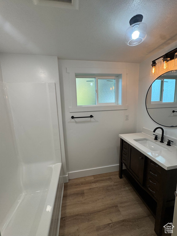 Bathroom with vanity, wood finished floors, plenty of natural light, baseboards, and a textured ceiling