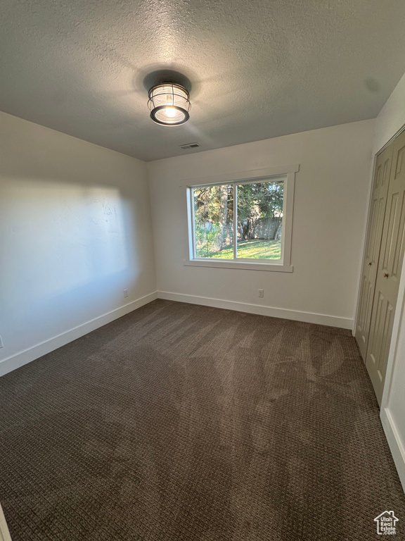 Unfurnished bedroom featuring a textured ceiling, baseboards, a closet, and dark colored carpet