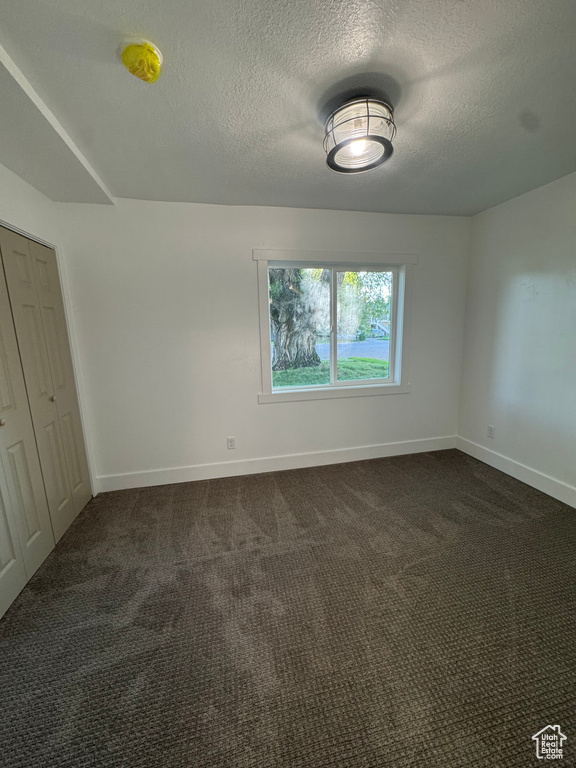 Unfurnished bedroom with baseboards, a textured ceiling, dark colored carpet, and a closet