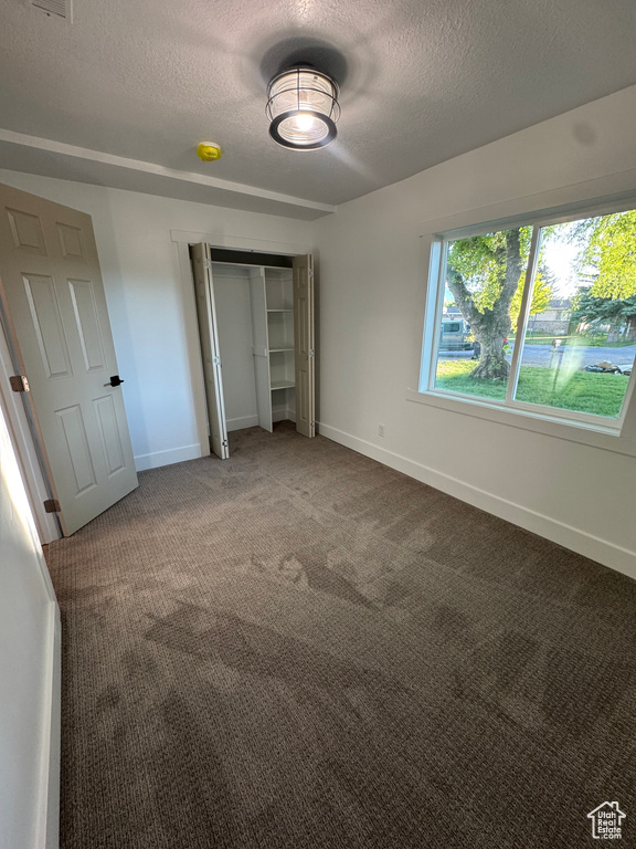 Unfurnished bedroom with a textured ceiling, carpet flooring, a closet, and baseboards