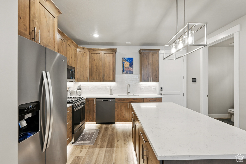 Kitchen featuring stainless steel appliances, light wood finished floors, a kitchen island, a sink, and decorative backsplash