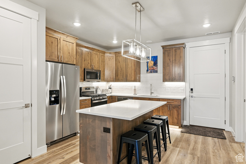 Kitchen with appliances with stainless steel finishes, light wood-type flooring, a breakfast bar, a sink, and tasteful backsplash