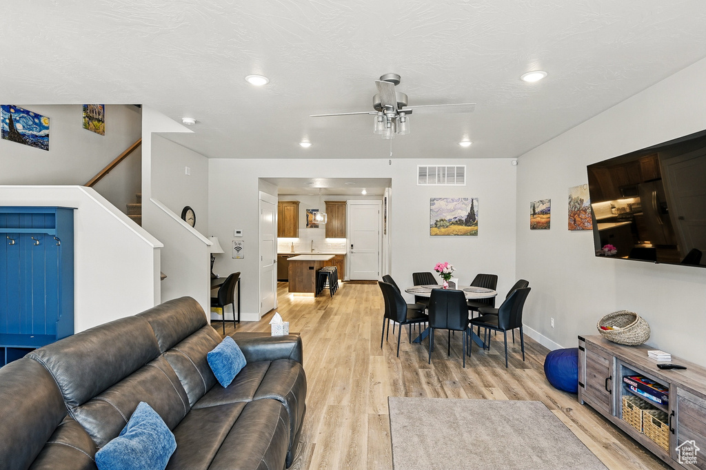 Living room featuring a ceiling fan, baseboards, light wood finished floors, stairway, and recessed lighting