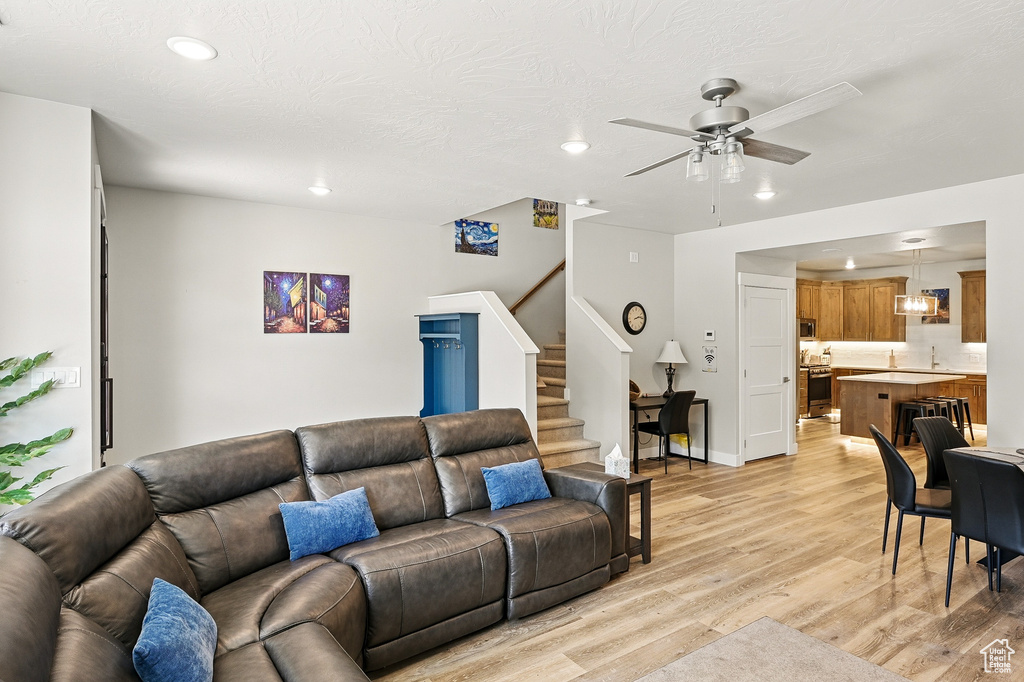 Living area with recessed lighting, light wood finished floors, ceiling fan, stairs, and baseboards