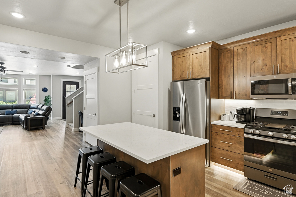 Kitchen featuring stainless steel appliances, light wood finished floors, open floor plan, a center island, and light countertops