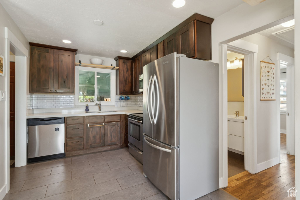 Kitchen with appliances with stainless steel finishes, a sink, light countertops, tasteful backsplash, and recessed lighting