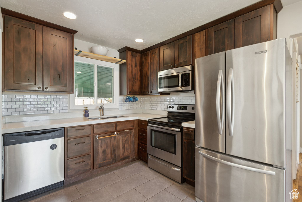 Kitchen with appliances with stainless steel finishes, a sink, light tile patterned flooring, light countertops, and decorative backsplash