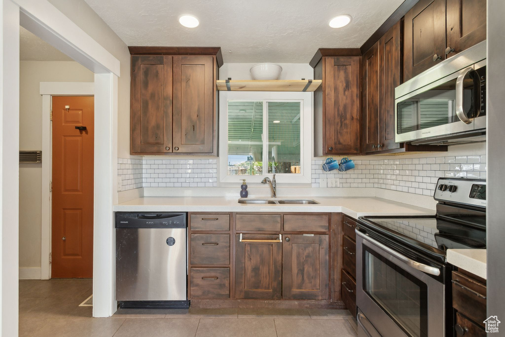 Kitchen with stainless steel appliances, a sink, decorative backsplash, light countertops, and recessed lighting