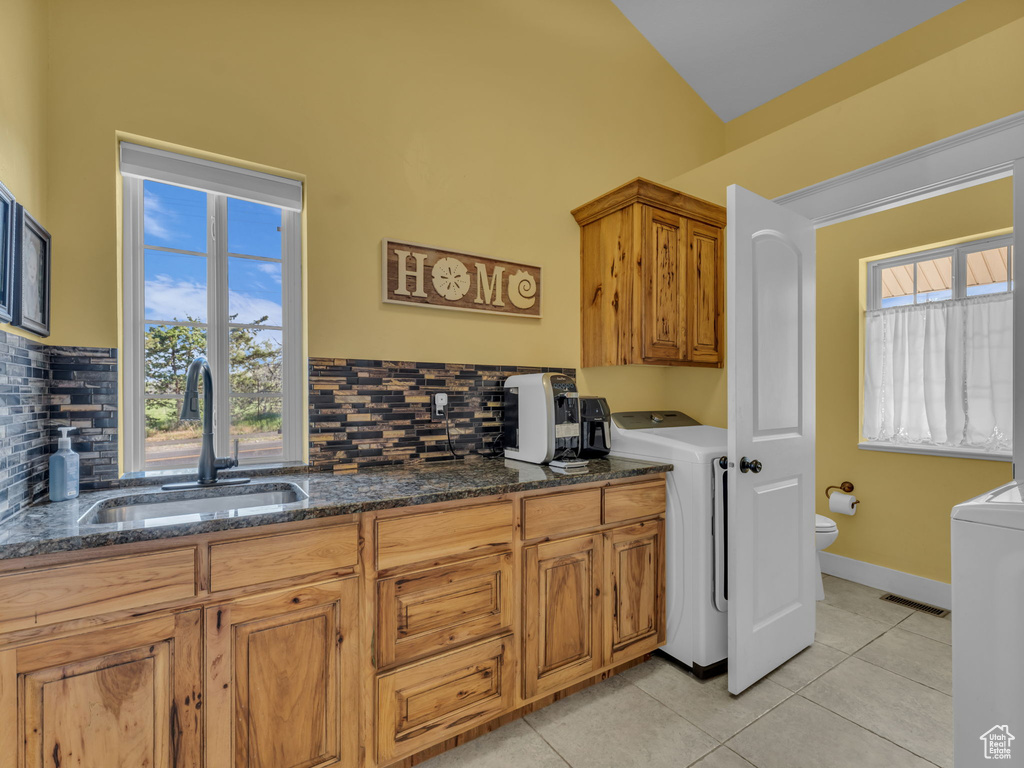 Kitchen with washer / clothes dryer, a sink, backsplash, and light tile patterned floors
