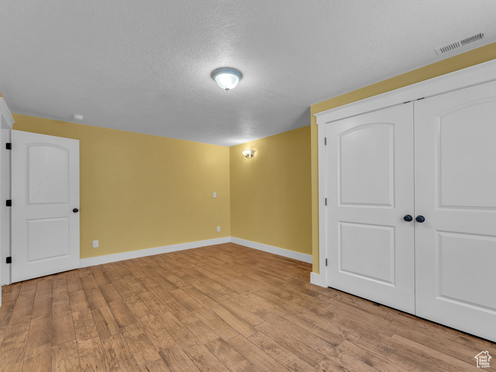 Basement with baseboards, light wood finished floors, and a textured ceiling