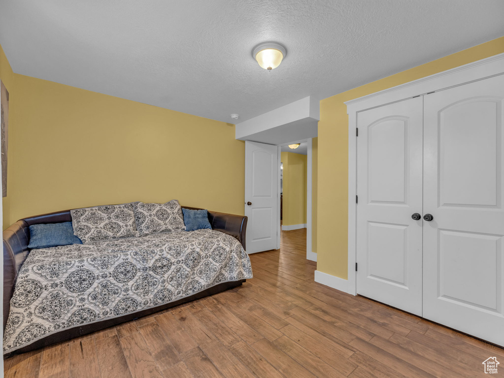 Bedroom with wood finished floors, a closet, a textured ceiling, and baseboards