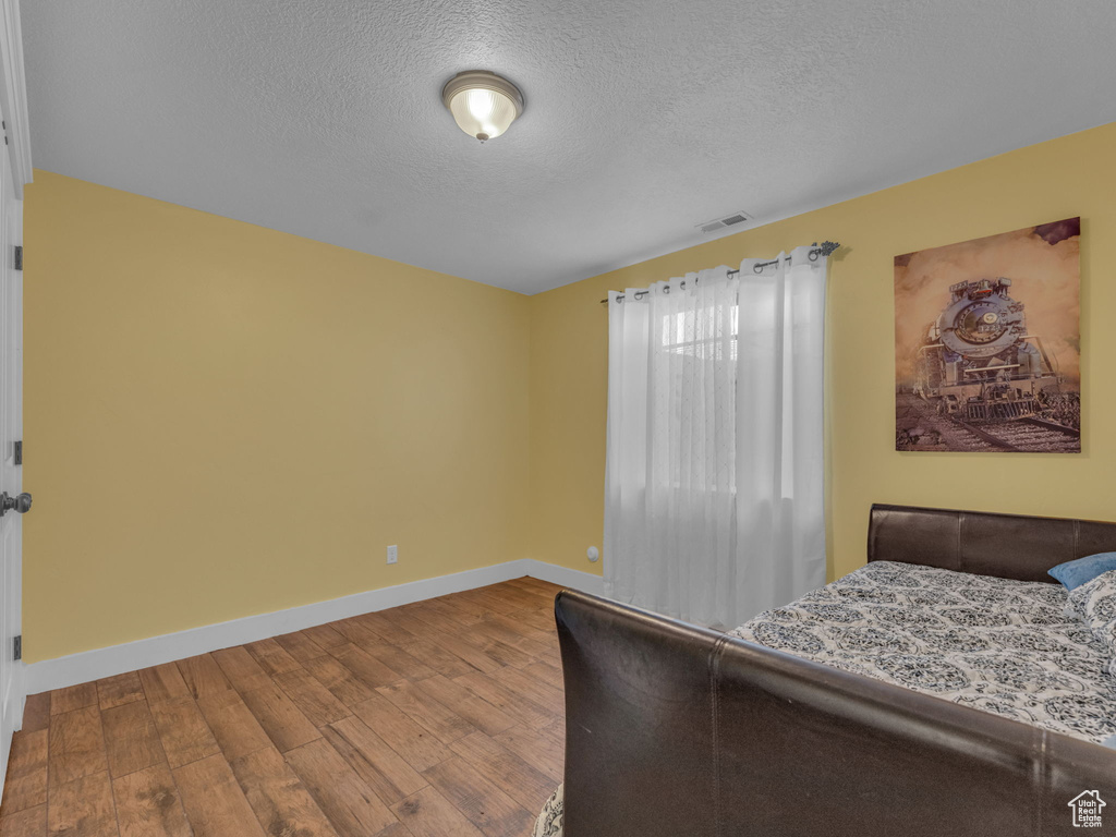 Bedroom with wood finished floors, baseboards, and a textured ceiling