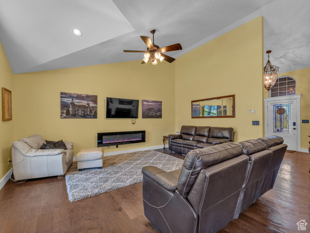 Living area with baseboards, dark wood-style floors, a glass covered fireplace, a ceiling fan, and a chandelier