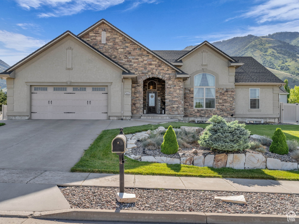 French country home with stucco siding, stone siding, an attached garage, driveway, and a mountain view