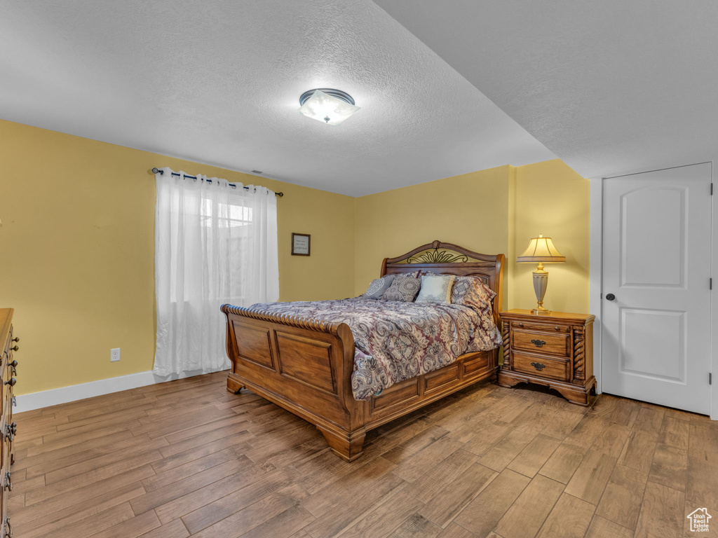 Bedroom with wood finished floors, a textured ceiling, and baseboards