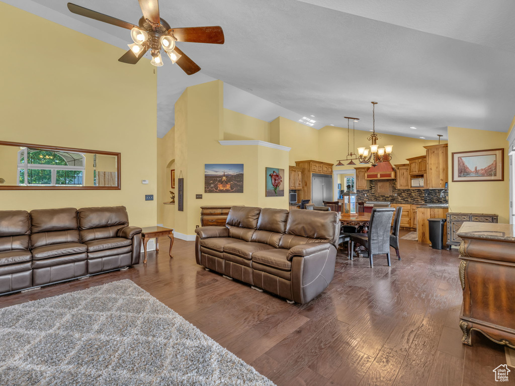 Living area featuring a ceiling fan, dark wood-type flooring, a chandelier, high vaulted ceiling, and baseboards