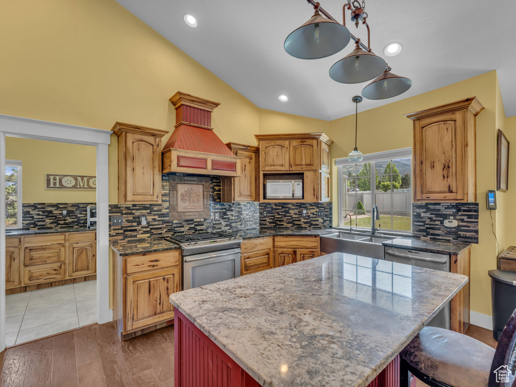 Kitchen featuring stainless steel appliances, a sink, vaulted ceiling, tasteful backsplash, and dark stone countertops