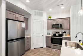 Kitchen with appliances with stainless steel finishes, a sink, light wood finished floors, light countertops, and pendant lighting