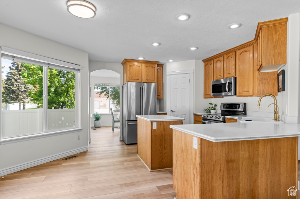 Kitchen with appliances with stainless steel finishes, a sink, a kitchen island, arched walkways, and light wood finished floors